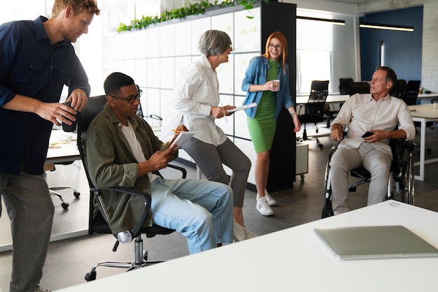 A diverse group of professionals collaborating around a conference table in a brightly lit office. They are reviewing documents and discussing strategies, with laptops and tablets scattered across the table. The atmosphere is collaborative and focused, reflecting a modern workplace environment.