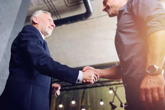 A close-up of two professionals shaking hands firmly at a networking event, symbolizing a strong connection being established. The background is blurred to keep the focus on the handshake and the individuals.