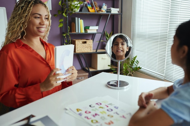 A person sitting at a desk, smiling confidently while practicing interview questions in front of a mirror in a home office setting.