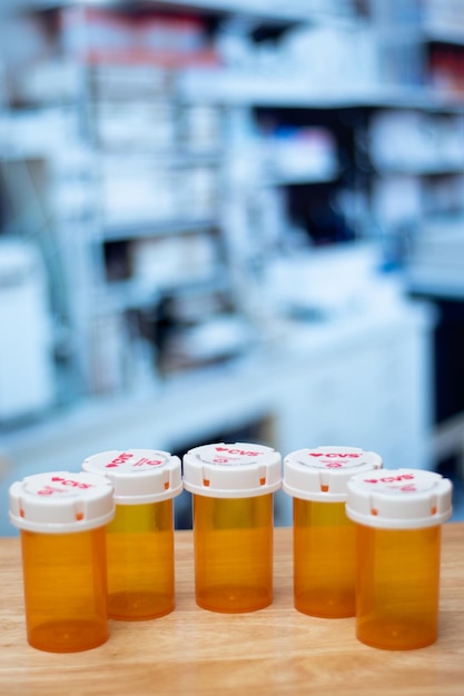 A close-up of prescription bottles with different price tags on them, illustrating the concept of price comparison. The background shows a blurred pharmacy setting to provide context.
