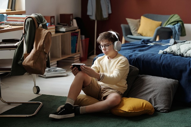 A pair of headphones resting on top of an open book, with a smartphone displaying an audiobook app in the background. The scene is set in a cozy living room.