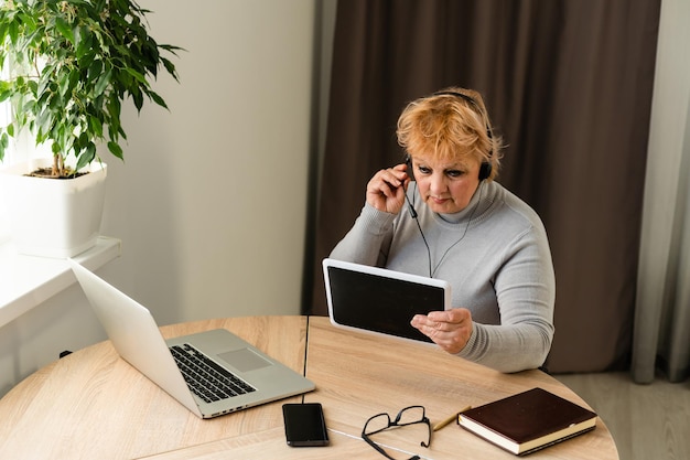 A person sitting at a desk, looking stressed and worried while reviewing financial documents and bills. A laptop is open with job search websites on the screen.