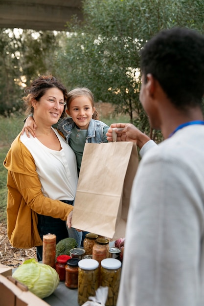 A family receiving groceries from a local food bank, demonstrating the impact of state-specific food and nutrition programs. The scene is warm and supportive, with volunteers assisting the family. The shelves are stocked with a variety of healthy food options.