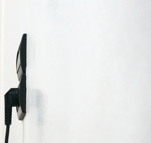 A close-up shot of an electric vehicle charger installed on the wall of a garage, with the charging cable plugged into an electric vehicle. The focus is on the charger and the connection, highlighting the installation process.