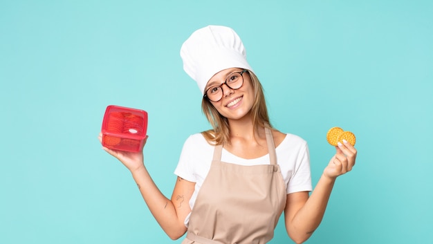 A person holding a small package of a new snack product, with a satisfied expression. The background shows a modern kitchen setting with colorful ingredients and cooking utensils.
